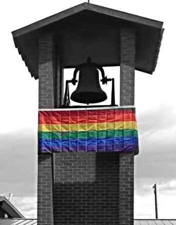 large rainbow flag hanging high up on a church bell tower