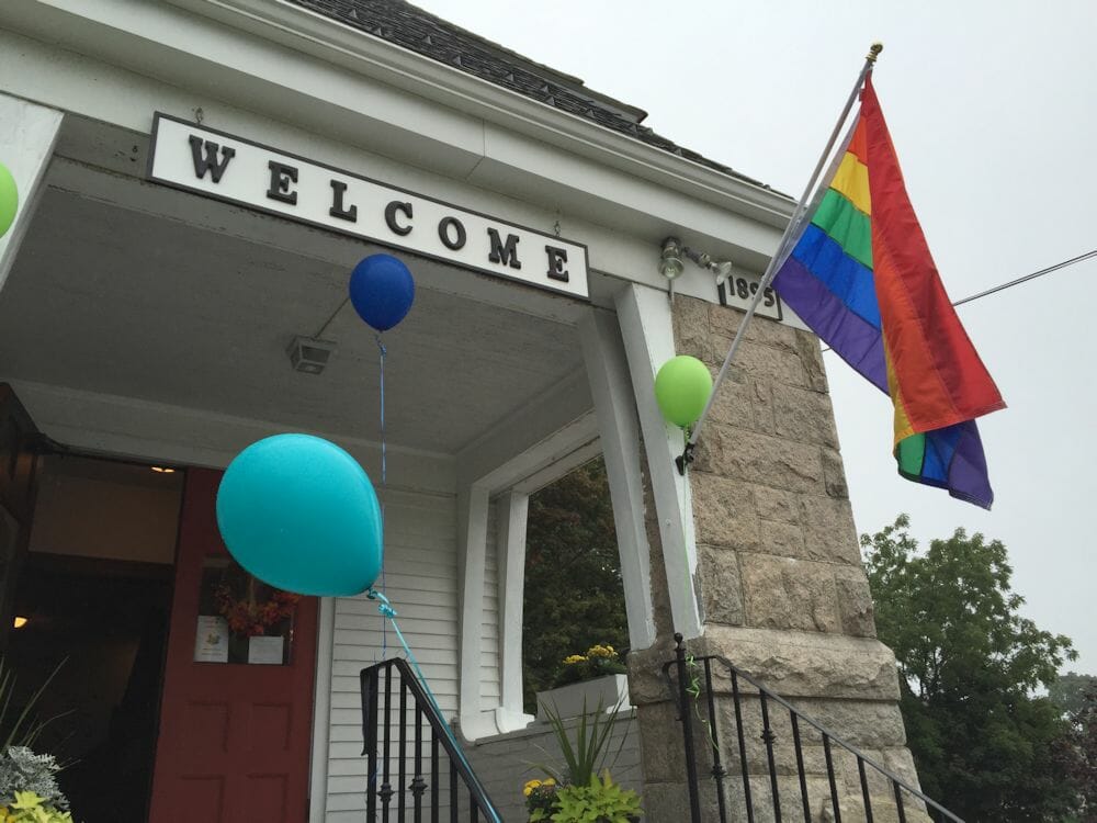 rainbow flag hanging from a church entrance next to a welcome sign