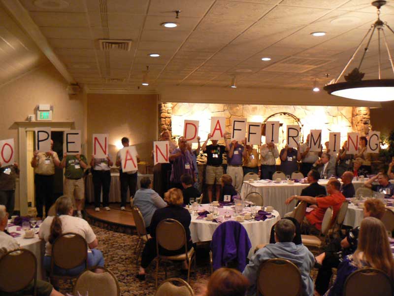 group of people in front of a conference room holding letters that spell "Open and Affirming"