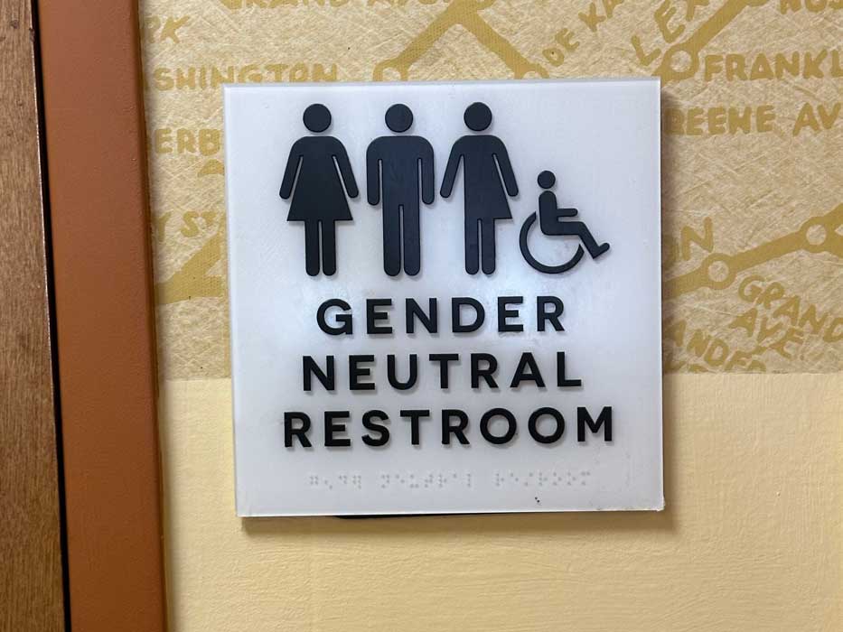 gender neutral restroom sign showing a person in a skirt, a person where only half has a skirt, a person without a skirt, and a person in a wheelchair