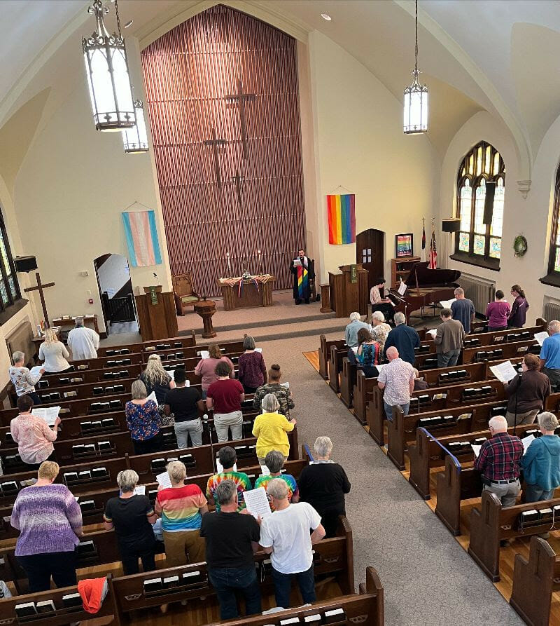 congregation in church sacntuary, pride flag hanging in the front